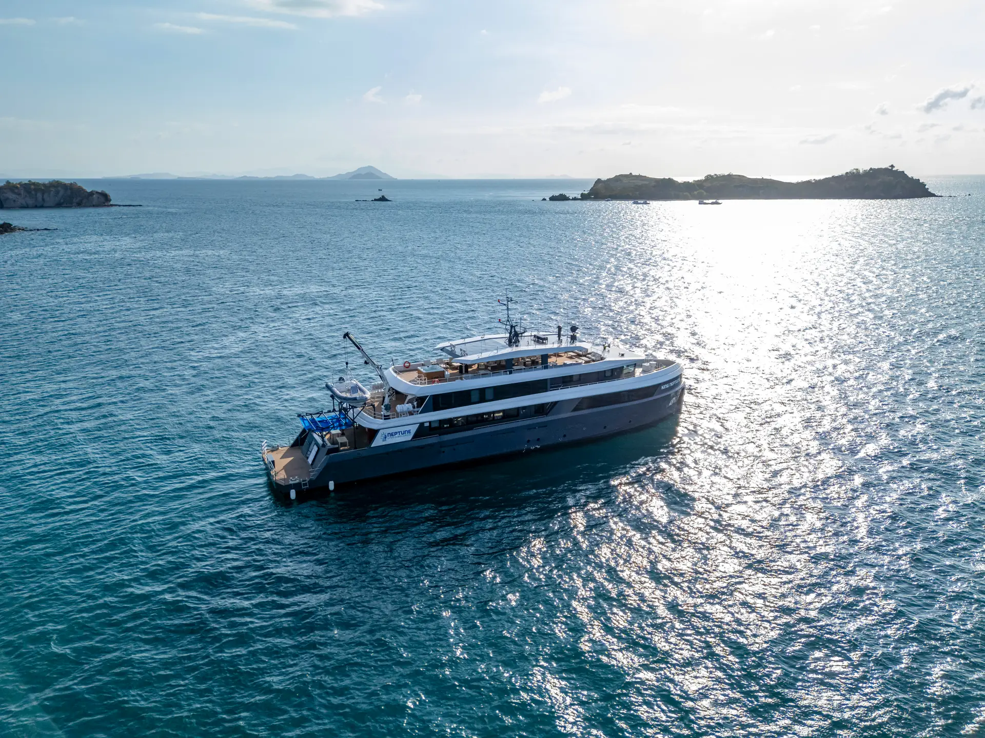King Neptune Auf einem Tauchsafari-Boot vor Anker vor einer grünen Insel in Indonesien