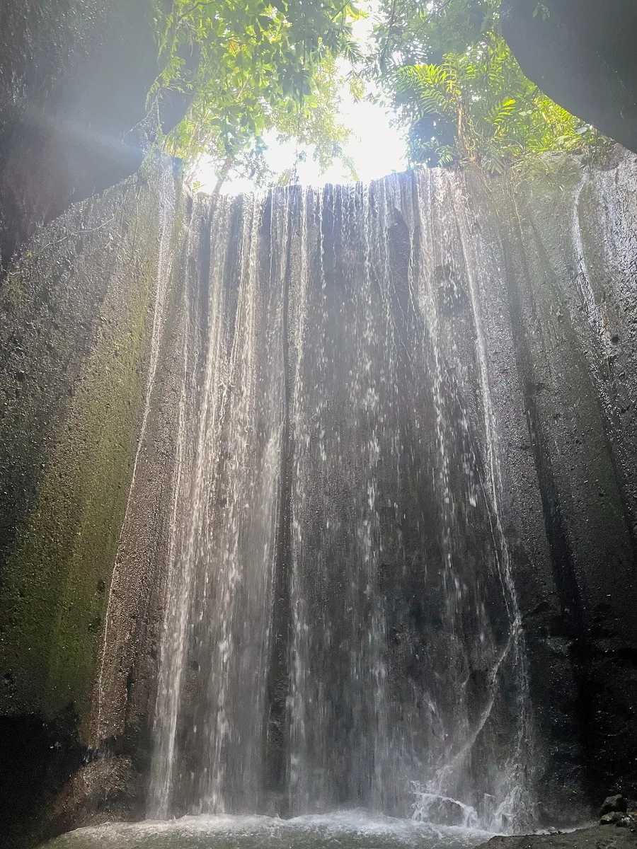 Tukad Cepung Waterfall in Bangli, Bali, water falling into a narrow rock canyon with sunlight streaming down through the opening above onto the falling water.