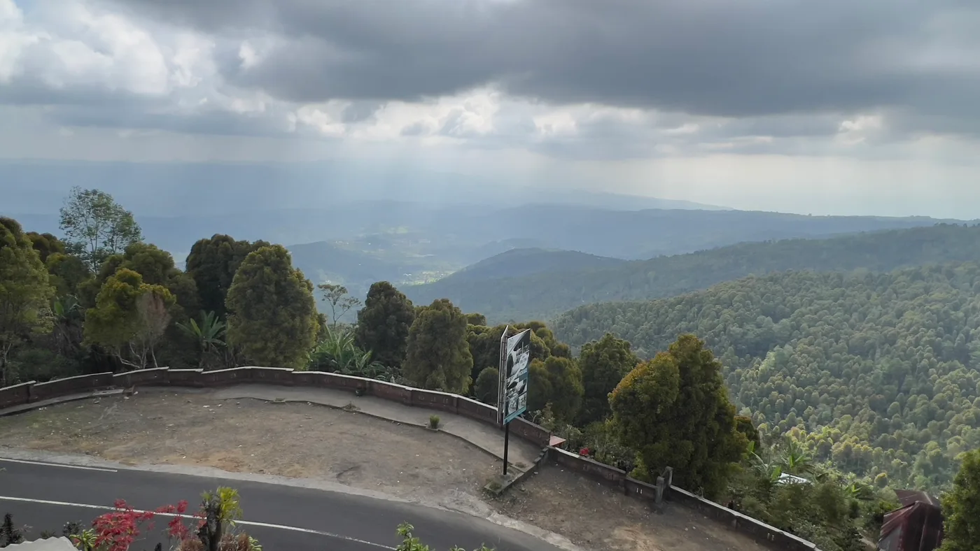 The view from Munduk over forested ridges dropping away towards the north coast of Bali, with shafts of light breaking through heavy cloud above the valleys.
